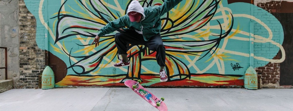 Skateboarder doing a trick in front of a spray painted industrial building