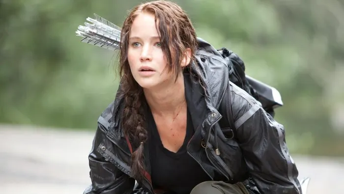 Hunger Games film still of Katniss Everdeen kneeling with a satchel of arrows on her back.