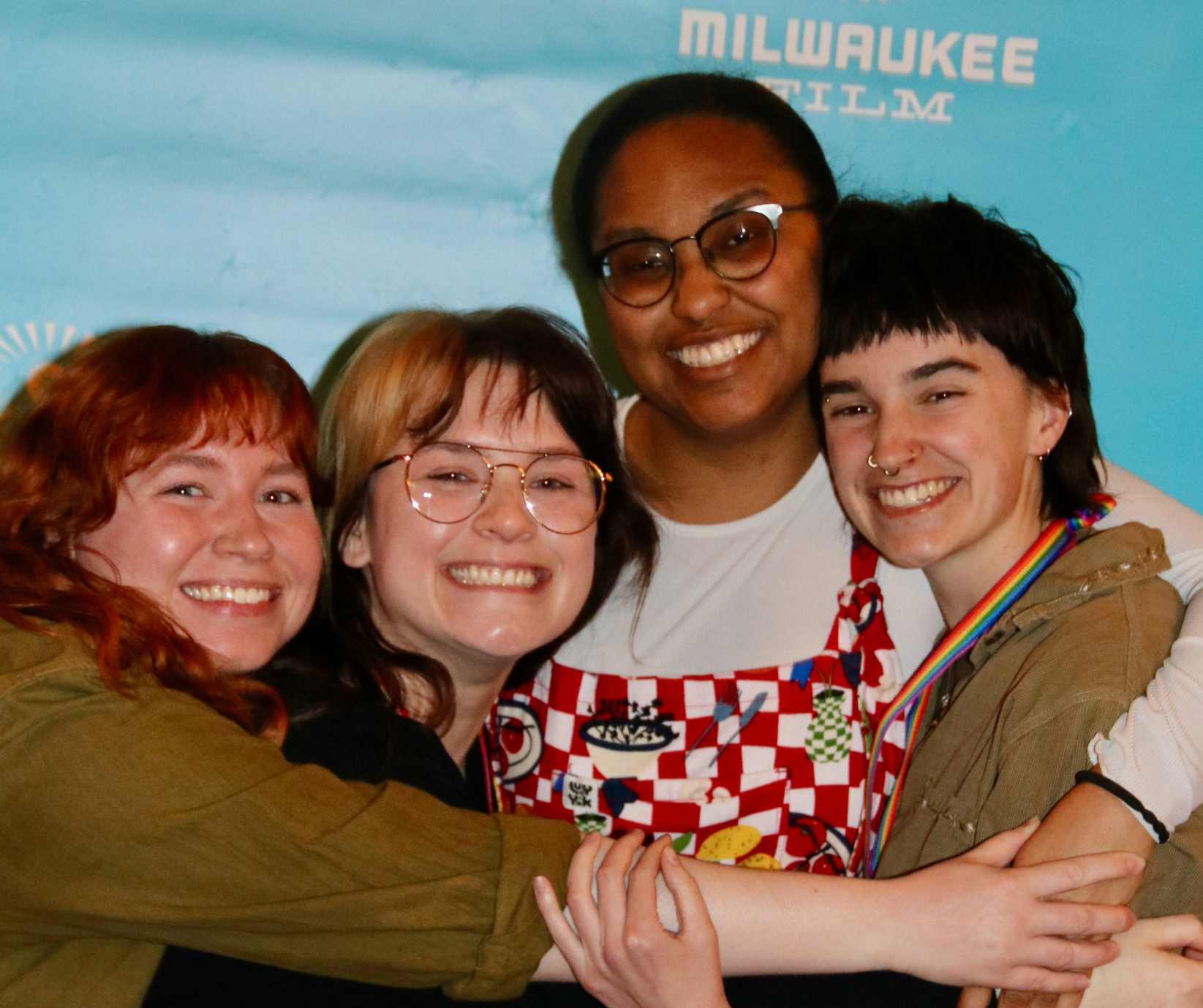 Four festival staff members hug in front of the 2025 milwaukee film festival backdrop