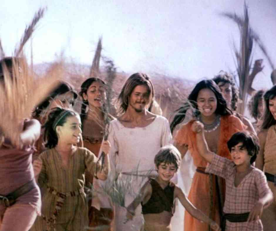 Jesus Christ Superstar Film Still Jesus walking through a crowd of women and children, he and the people in the image are smiling as they walk.