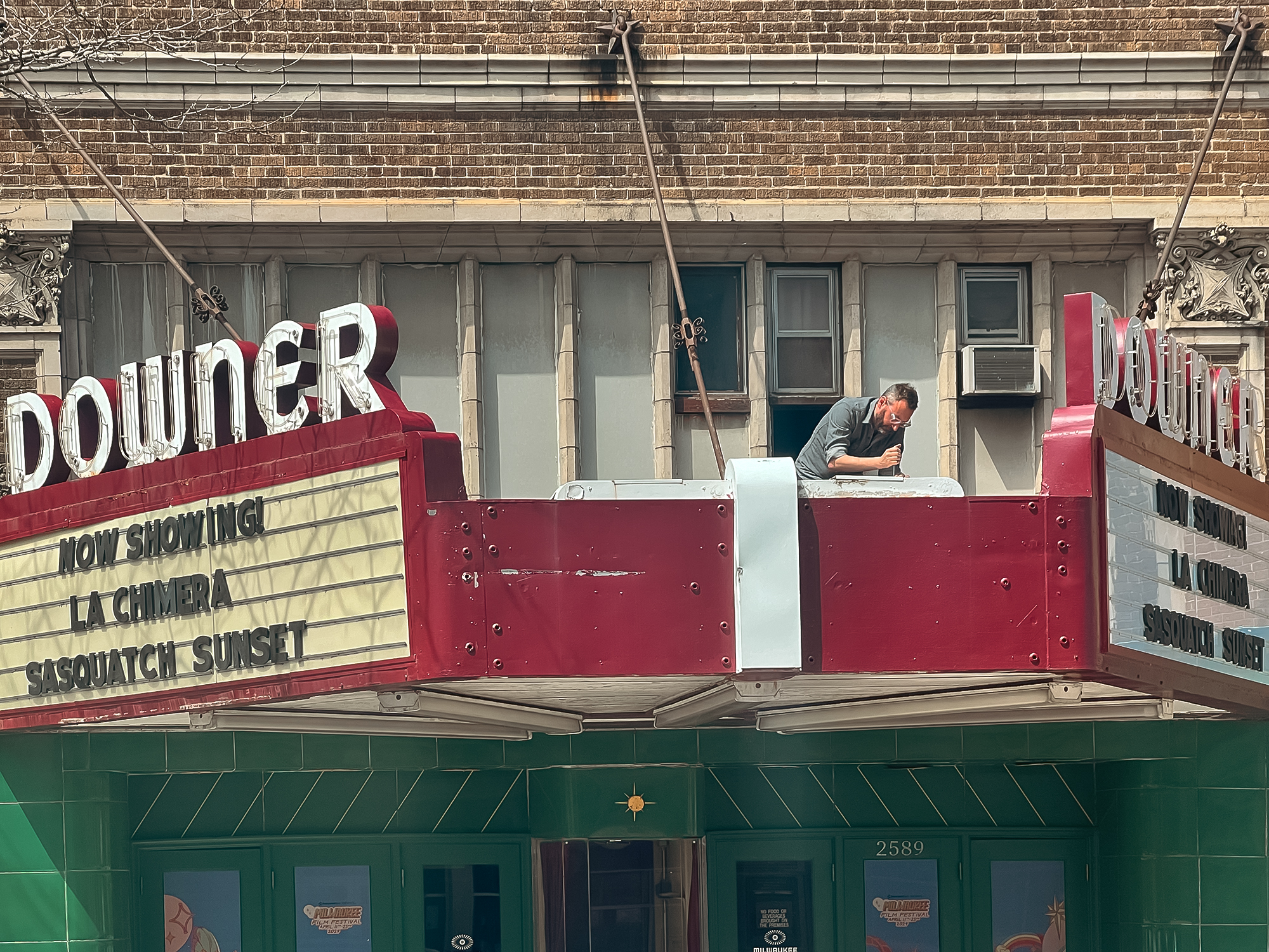 A man stands on top of the marquee at the Downer Theatre, repairing it.