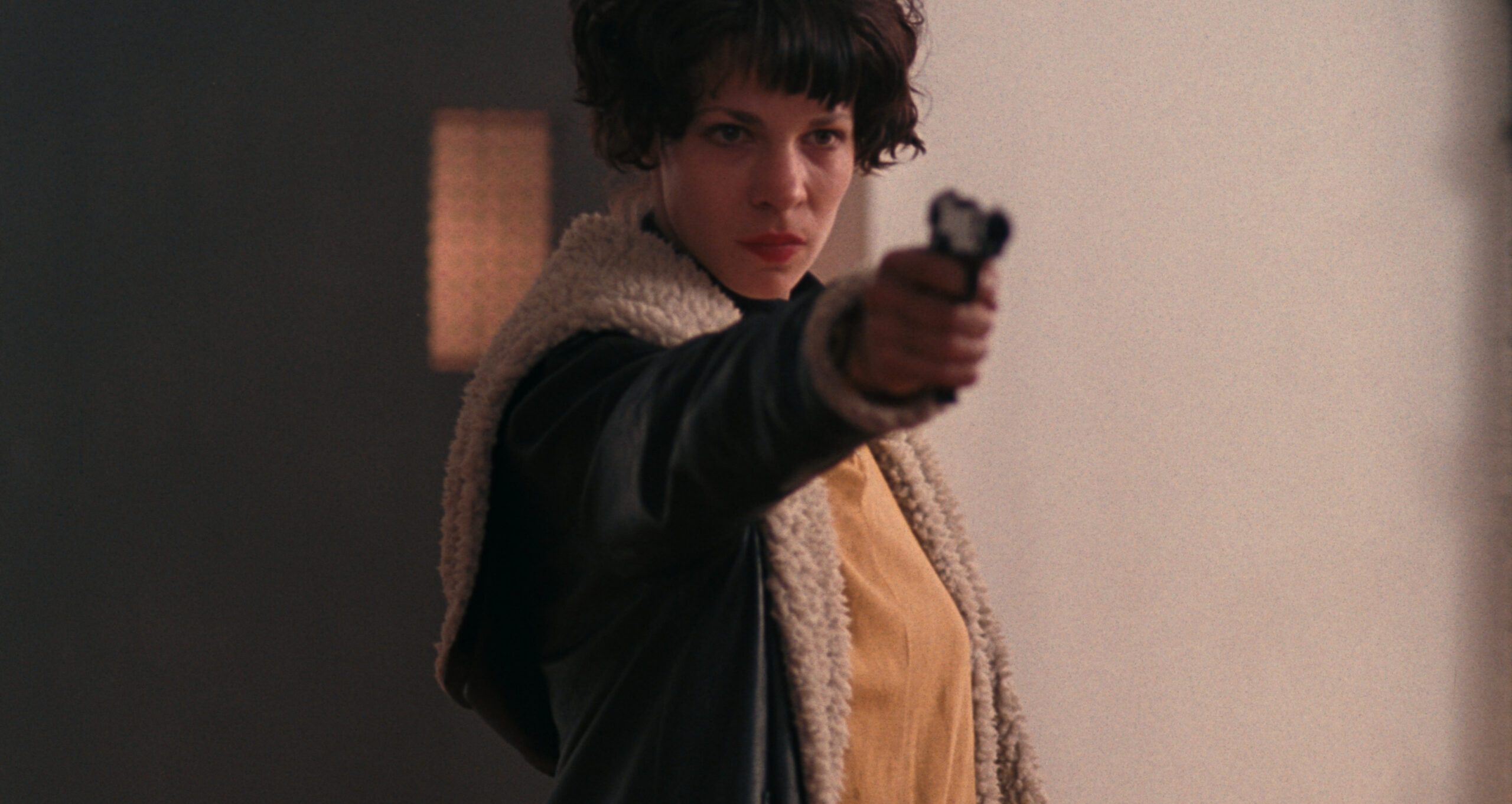 I Shot Andy Warhol Film Still A woman with short curly hair with a raised arm points a hand gun.