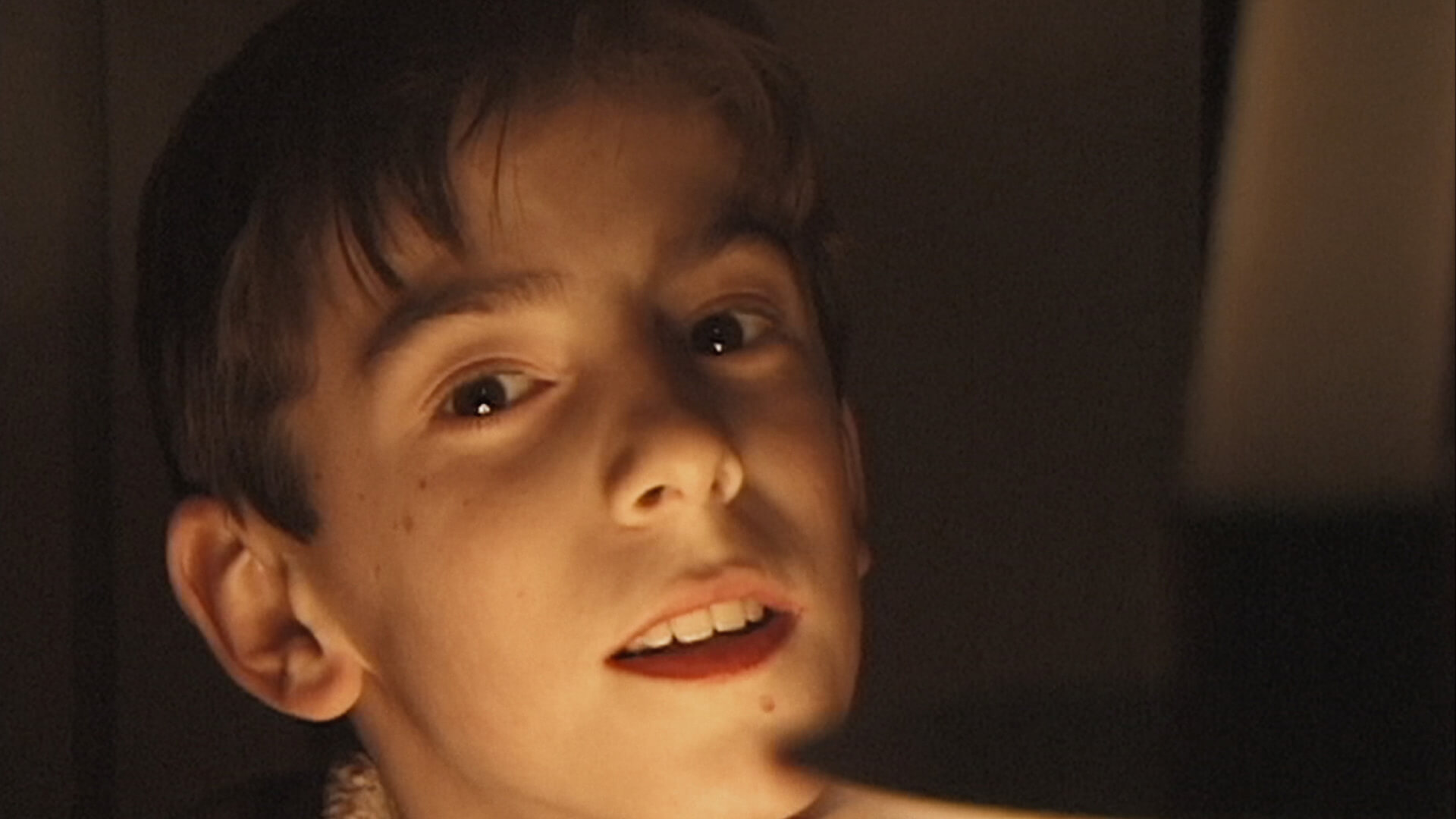 Remake Film Still A young boy looks at the camera with his face barely lit by a flashlight.