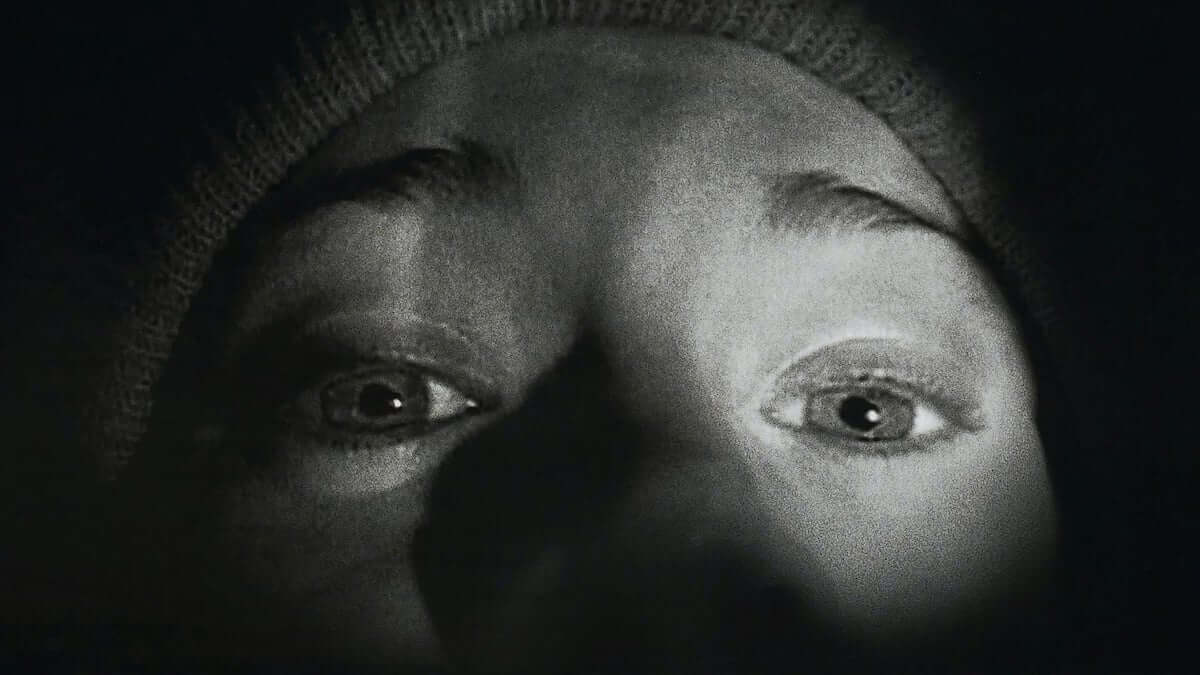 Blair Witch Project Film Still Black and White photo of a pair of eyes looking frightfully towards a flash