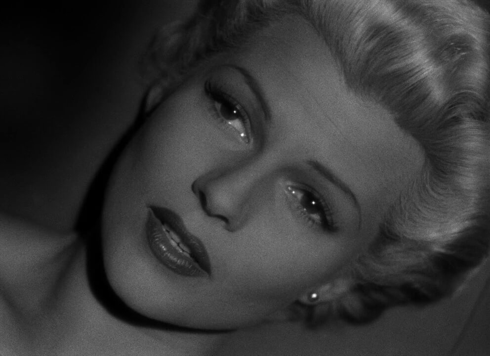 The Lady From Shanghai film still Black and white close up on a woman's face, she has light colored hair and a colorful lip on, she looks emotional