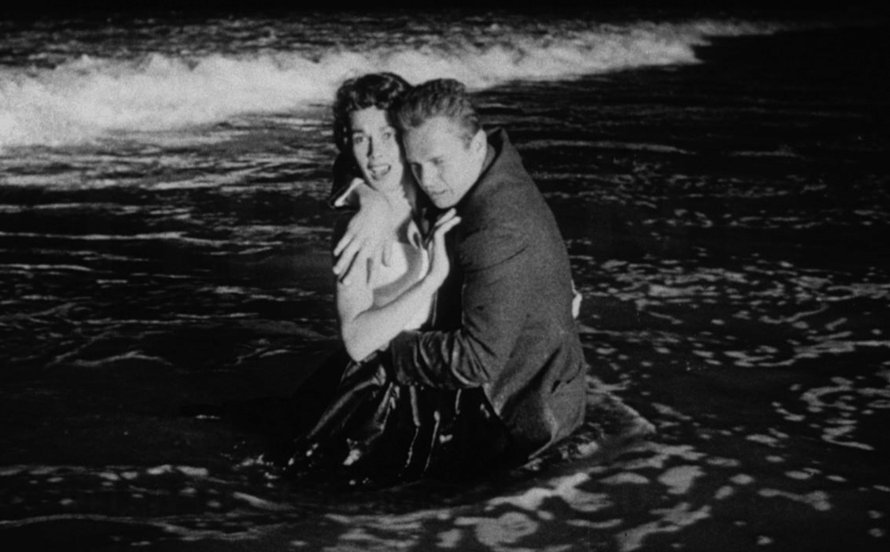 Kiss Me Deadly Film Still Black and White medium shot of a man and a woman holding each other while soaking wet on a beach